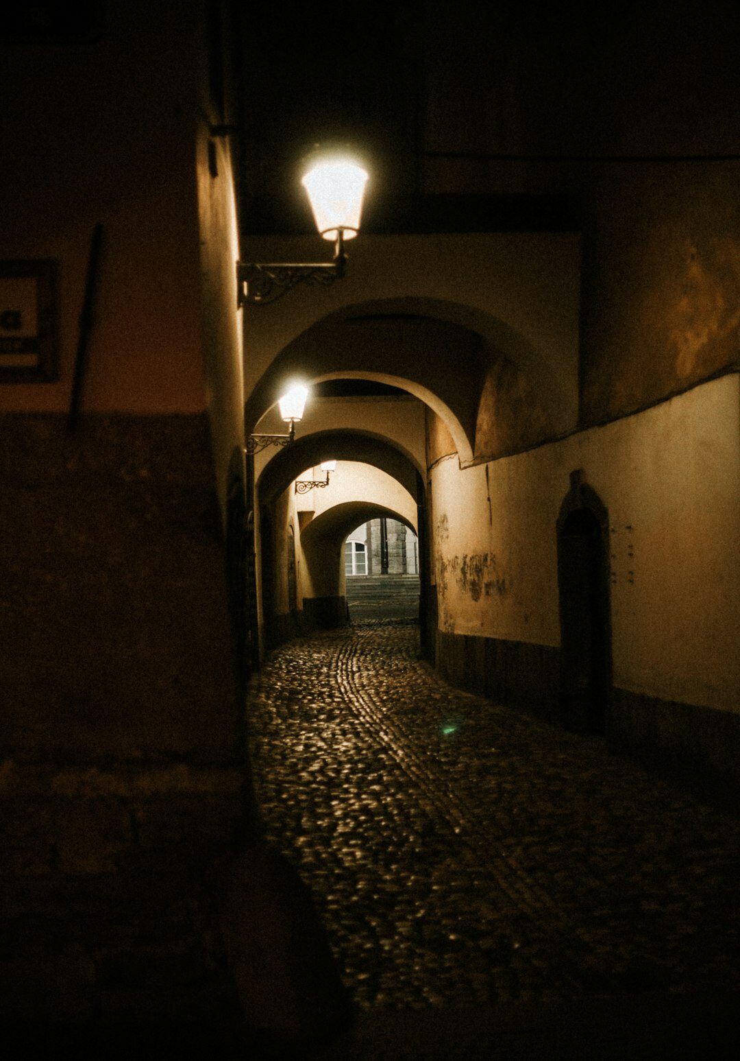 Foggy cobblestone street in an old European town at night with a single glowing lamp